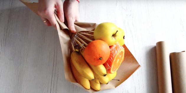 Положите букет из фруктов своими руками по диагонали на бумагу и заверните низ