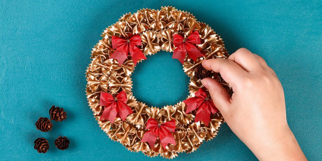 С помощью клея прикрепите к венку бантики и шишки
