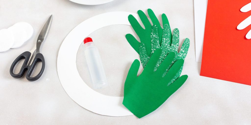 По кругу приклейте ладони к основе для венка. Сверху прикрепите банты, бусины и другой декор по своему вкусу