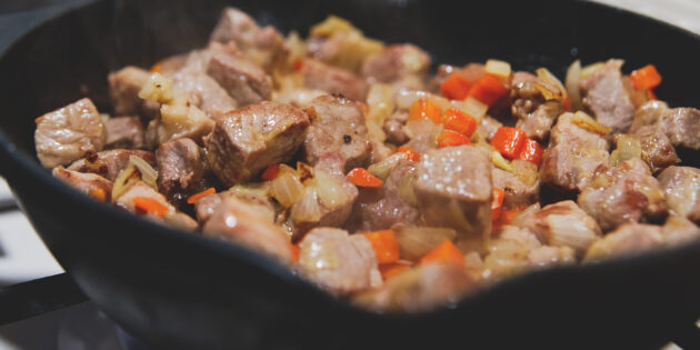 Свинина в пиве: отправьте овощи в сковородку к мясу, убавьте огонь до среднего и готовьте всё вместе, пока морковка с луком не станут мягкими